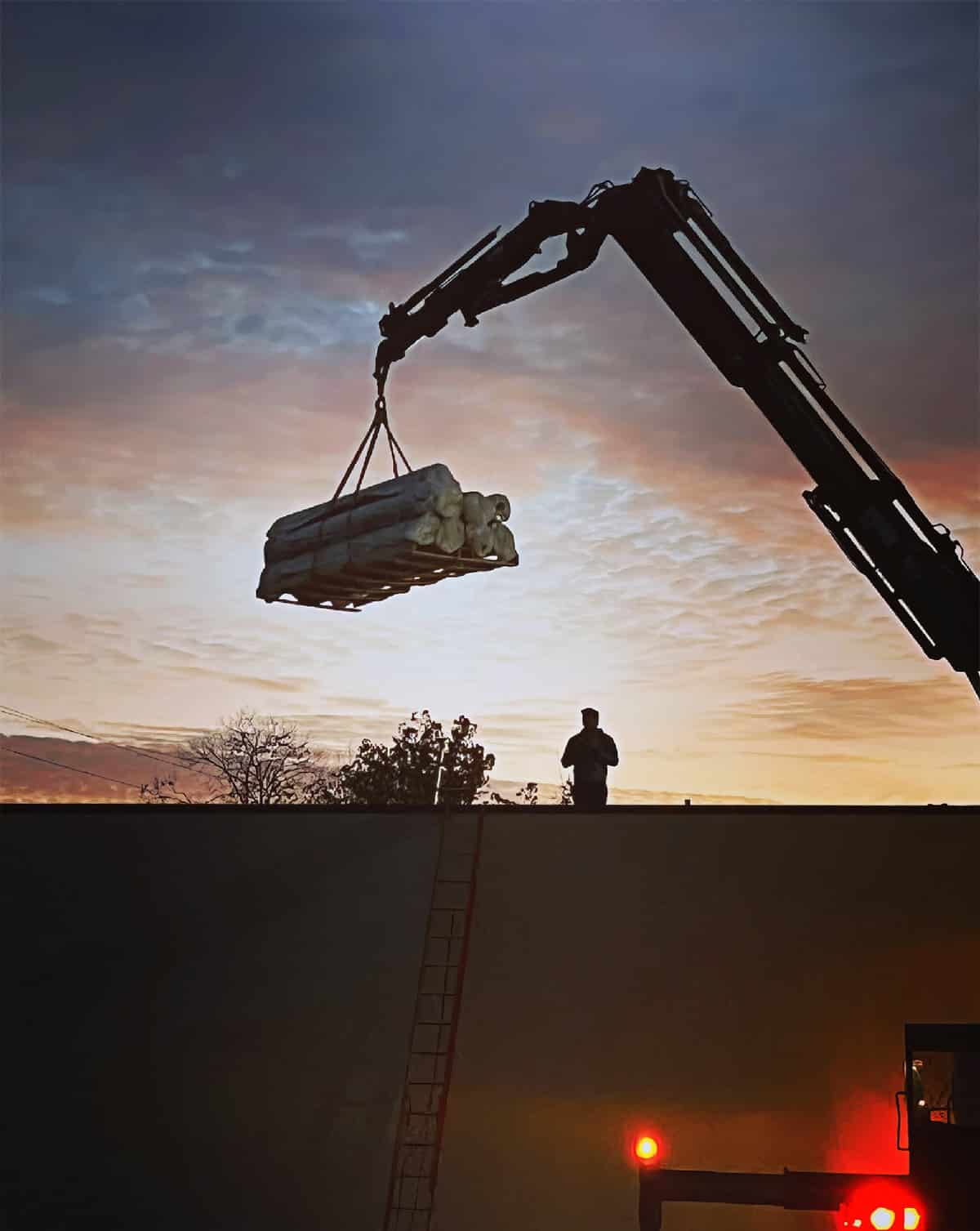 Flat roofing material is lifted onto a building at dusk.