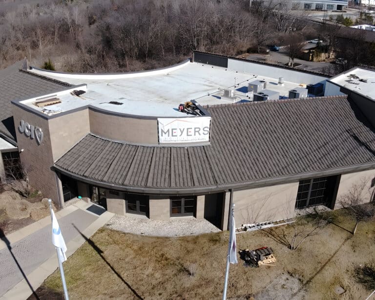 Aerial view of a JCI building with a flat white roof, tile-style edge, and a Meyers commercial flat roofing banner.