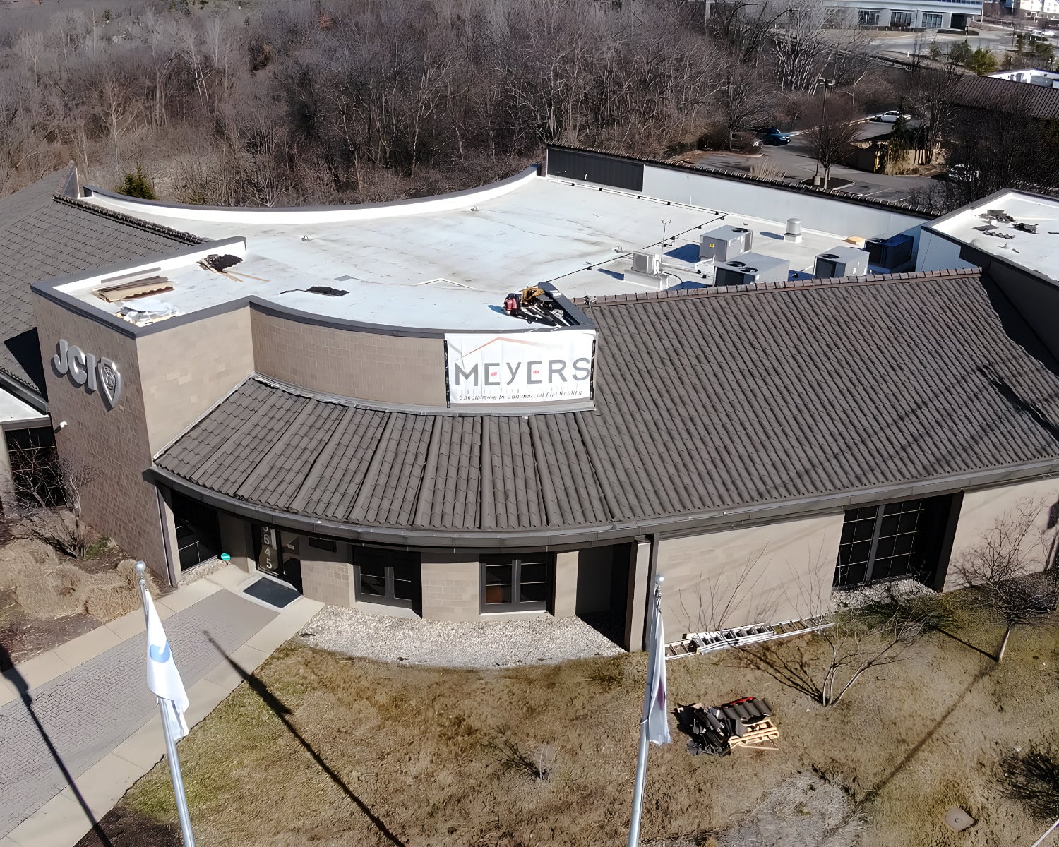 Aerial view of a JCI building with a flat white roof, tile-style edge, and a Meyers commercial flat roofing banner.