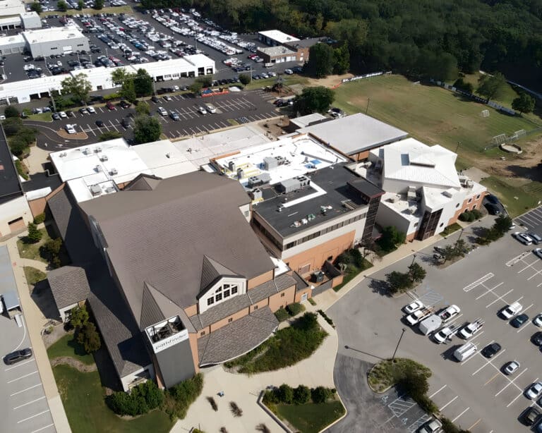 Aerial view of the Pathfinder church campus with mixed pitched and flat roofs, parking lots, and a school field beyond.