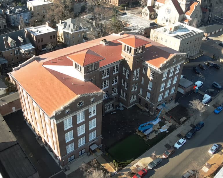 Aerial view of a brick building with a terracotta tile roof and tower, with a boom lift working in the courtyard.