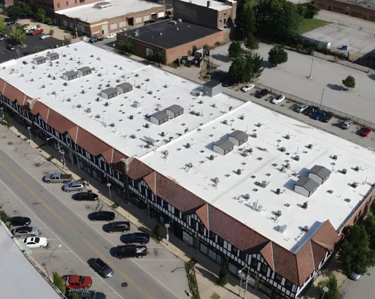 Aerial view of a Tudor-style commercial building with a large white flat roof, rooftop HVAC units, and street parking.