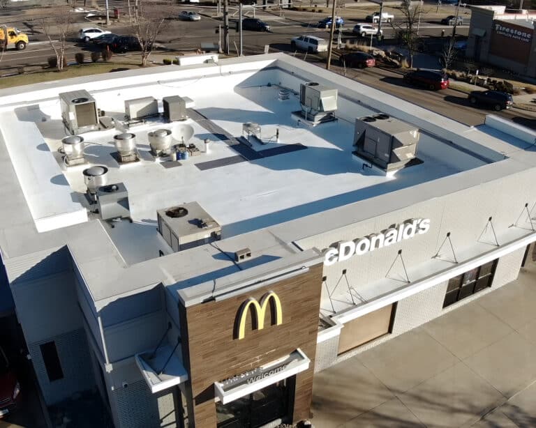 Aerial view of a McDonald's restaurant with a white flat roof, rooftop HVAC units, and a busy road behind.