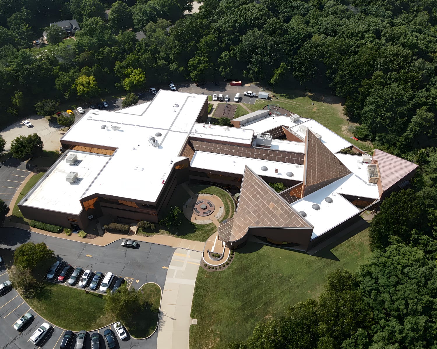 Aerial view of a large angular building with white flat roofs and a central courtyard, surrounded by dense forest.