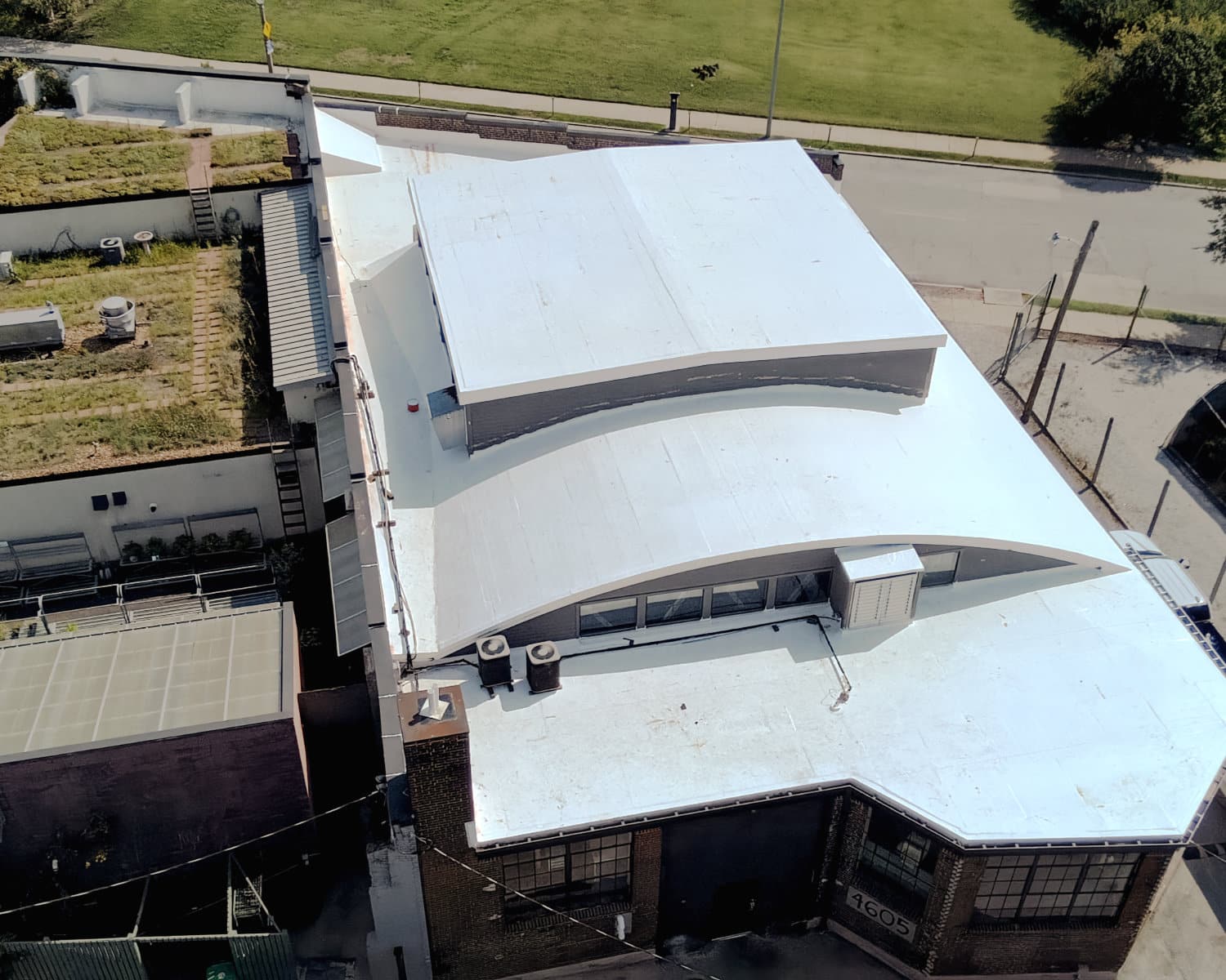 Aerial view of a brick building with a white flat roof, curved raised section, and a neighboring green roof.